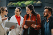© qunica.com - Four people come together outside a modern backdrop, exchanging ideas with a tablet and notebook. The scene conveys collaboration, networking, and friendly, productive teamwork in a casual setting.