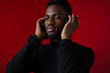 © SHOTPRIME STUDIO - A focused young Black man in a black turtleneck, enjoying music with headphones against a vibrant red background, exuding calmness and concentration, ideal for themes of relaxation and mindfulness