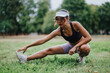 © qunica.com - A fit woman stretches on the grass in a park, wearing a black sports bra and lavender shorts. She reaches toward her shoe, captured in a dynamic outdoor workout moment.