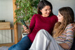 © NDABCREATIVITY - Happy pregnant mother relax on sofa with teenage daughter, hold mobile phone, chat in social media