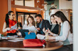 © qunica.com - A diverse group of people gathers around a round table, reviewing documents and sharing ideas. Laptops, tablets, and coffee create a dynamic, collaborative workspace vibe.