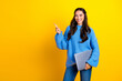 © deagreez - Young mixed race woman in blue sweater holds laptop and points to the side against a bright yellow background