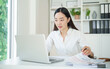 © matinee - Businesswoman analyzing financial reports and typing on laptop computer at modern home office.