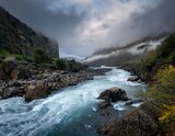 powerful river surges through rocky terrain shrouded in mist under a dramatic sky evoking nature s raw force