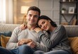 © Vasiliy - A happy young couple relaxing on the couch at home. An affectionate man and woman smile and embrace in their cozy living room
