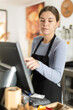 © JackF - Young female cashier in apron at cash register in cafe
