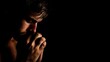 © Photo_hub - Young man praying with hands clasped in dark room with low key lighting