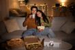 © Prostock-studio - Two people relax on a couch at home, enjoying a fun evening together. They watch a movie from a projector while sharing pizza and popcorn, creating a cozy atmosphere filled with joy.