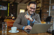 © Miljan Živković - Businessman working remotely smiling in a modern cafe
