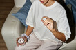© Seventyfour - Young adult woman sitting on sofa holding glass of water in one hand and capsule pill in other hand, preparing to take medication at home