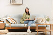 © Pixel-Shot - Young woman using laptop on grey sofa near light wall at home
