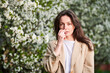 © anatoliy_gleb - Woman allergic using medical nasal drops, suffering from seasonal allergy at spring in blossoming garden. Young woman treating runny nose in front of blooming tree outdoors. Spring allergy concept.