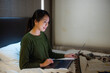 © leungchopan - Woman working on laptop sitting on bed