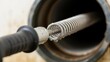 © Mano - Professional drain auger extending into a dark pipe clearing blockage with water droplets
