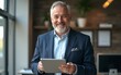 © David - Older smiling business man holding tablet standing in office. Middle aged happy businessman manager investor using tab computer, mature male executive looking at camera at work. Portrait.