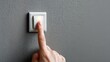 © OngCaLucK - Close-up of a Hand Pressing a Modern Light Switch on a Gray Wall in a Contemporary Interior Space for Home Design or Renovation Purposes