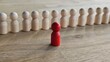 © Nadzeya - A red figure in a row between wooden figures of people. Individuality, uniqueness, leadership and distinctiveness concept