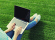 © rohappy - Female hands woman working with laptop, blank black screen in the park on green grass background