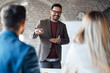 © Novak - Professional businessman giving a presentation to colleagues on a whiteboard in a modern office