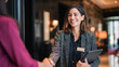 © Andrey - A smiling professional hotel receptionist in a grey blazer shakes hands with a guest in a lobby, holding a digital tablet. Shallow depth of field with warm indoor lighting.