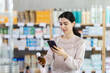 © JackF - Woman in a sweater scans the barcode of medicated syrup for cough and cold symptoms on mobile. Customer in a European pharmacy uses a mobile phone to pay for goods