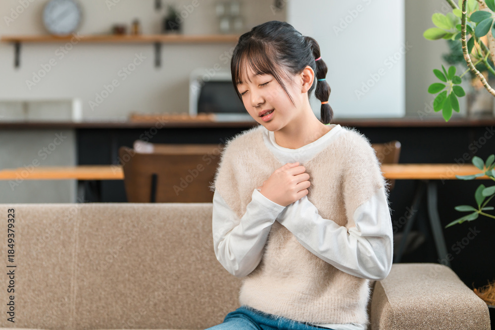 A girl in elementary and middle school sitting on a sofa at home ...