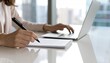 © Dompet - Woman's hands writing notes near laptop, blurred office view