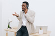 © SHOTPRIME STUDIO - Confident young African American man wearing smart casual outfit talking on mobile phone in modern office space, gesturing with hand, smiling, isolated on plain white background, professional