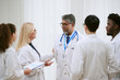 © AnnaStills - Group of diverse young adult and middle aged doctors including Caucasian woman, Asian man, Black man and South Asian man standing together discussing medical documents in hospital setting