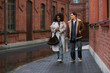 © DragonImages - Young adult Black woman holding bouquet of flowers, walking beside young adult Caucasian man on city street, smiling and talking during romantic date in urban setting