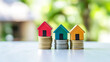 © Elena - Three miniature houses colorful roofs coin stacks green nature background. Concept of property investment, real estate growth, savings, and housing portfolio.