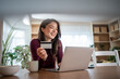 © Migma_Agency - Woman holding credit card while online shopping at home