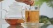 © kinomaster - A close up of a woman hand stirring herbal tea in a glass cup with a teaspoon on a glass table in the kitchen.