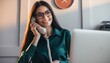© Rifqi - Smiling young female executive wearing glasses talks on a corded landline phone in a warm office setting, concept for corporate communication, customer service and business efficiency