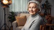 © Lexi - Elderly woman smiling while sitting on a chair in a cozy interior - Concept of People