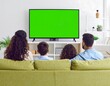 © Fatonah - Family watches television with a green screen on a sofa. A white bookshelf is behind them with decor