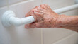 © A2Z AI  - Close up of a senior woman's hand gripping a white support bar in a tiled bathroom.  This assistive technology helps aging adults maintain independence and safety while bathing.