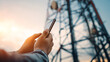 © A2Z AI  - Person interacting with a smartphone in front of a large transmission tower at sunset. Focus on connection and technology with the tower symbolizing communication networks.