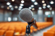 © Yurij - Macro view of a microphone on stand ready for speech or presentation with blurred auditorium seats and lights in the background during an event or conference