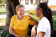 © StockMe - Diverse senior women friends enjoying outdoor conversation, one woman smiling and looking at her friend, feeling happy and supported by a warm touch on the shoulder