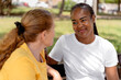 © StockMe - Smiling african american woman engaging in a warm conversation with a friend outdoors, sharing moments of diverse friendship and active listening in a park setting