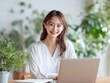 © Jumpei - 観葉植物のある明るい室内でノートパソコンを使いながら笑顔で仕事をする女性