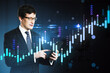© Who is Danny - Businessman analyzing financial market data on smartphone with digital stock chart interface on dark background, concept of currency trading.