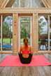 © boomeart - Woman practices yoga inside a wooden cabin with a view of the garden in the afternoon