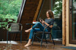 © boomeart - Barefoot woman sits outside a wooden house and uses a mobile phone while relaxing