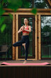 © boomeart - Woman practicing yoga on a mat outside a wooden house during daylight