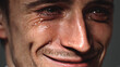 © Jiraporn - Smiling man hides pain behind joyful expression concept. A close-up of a man smiling despite tears, reflecting deep emotion.