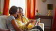 © stockbusters - Two girls looking tablet sitting apartment sofa closeup. Smiling women choosing