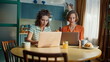 © stockbusters - Morning girls watching laptops sitting kitchen table. Women friends computers