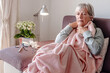 © luciano - Elderly Caucasian woman with severe cold and fever symptoms, similar to seasonal flu or pollen allergy - woman on the couch at home covers herself with a blanket because she feels cold